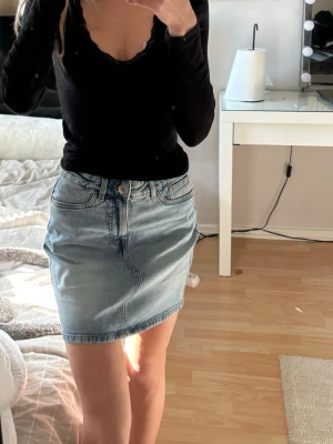 Ljusblå jeanskjol i klassisk modell - Trendig ljusblå jeanskjol med femficksmodell och normal midja. Kjolen har dragkedja och knapp framtill samt två bakfickor. Perfekt basplagg till garderoben och lätt att matcha med olika toppar. 