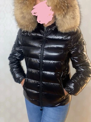 Svart glansig dunjacka med pälshuva - Snygg glansig figursydd dunjacka med pälskrage i 100% äkta päls från vivanilla. Haft den några år men i bra skick, finns något märke (se bild) utöver det inget annat märkvärdigt. Ordinariepris, 3799kr