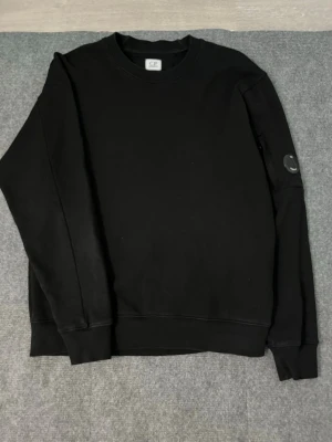 C.P. Company Sweatshirt – Size M - Selling this clean and stylish C.P. Company sweatshirt in excellent condition ✨ It has been worn only a few times, so it’s still very clean, well‑kept, and looks great. The item is 100% authentic, featuring the signature sleeve lens detail.  Size: M Color: Black ⚫️  Measurements:  Length: 67 cm Width (pit to pit): 53 cm  I will ship it immediately after purchase 📦💨