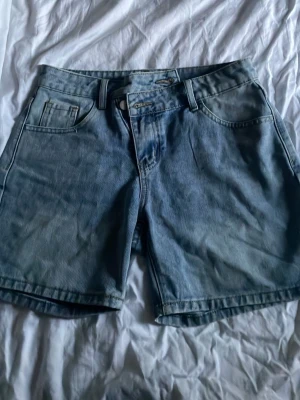 Ljusblå långa shorts med dragkedja - Klassiska ljusblå jeansshorts i rak modell. Perfekta för sommaren och har en avslappnad passform. Dem har en speciell knapp omvändning som är sne vilket gör den lite unik! Snygga att matcha med en enkel t-shirt eller hoodie. 
