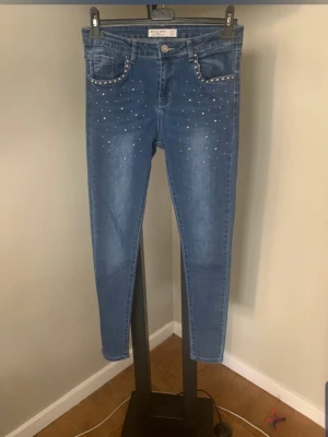 Blå jeans med nitar från Hello Miss - Snygga blå skinny jeans från Hello Miss med silverfärgade nitar längs fickorna och framtill på benen. Klassisk femficksmodell i stretchigt denimtyg. Perfekta för dig som vill ha en cool och trendig look.