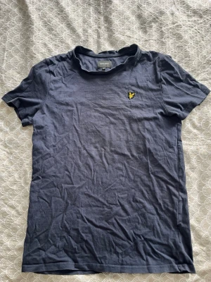 Mörkblå t-shirt från Lyle & Scott - Snygg mörkblå t-shirt från Lyle & Scott med klassisk gul logga på bröstet. T-shirten har rund hals, korta ärmar och är gjord i mjuk bomull. Perfekt basplagg till garderoben.