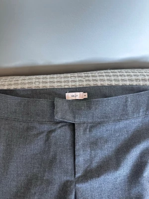 Grå kostymbyxor från Nelly - Snygga grå kostymbyxor från Nelly med rak passform och klassisk midja. Byxorna har en stilren look och är perfekta till en dressad outfit. Tillverkade i ett mjukt tyg som ger en skön känsla hela dagen.