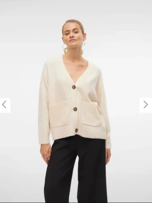 Krämvit kofta med stora knappar - Mysig krämvit kofta med v-ringning och stora bruna knappar framtill. Två rymliga fickor på framsidan och ribbade muddar vid ärmslut och nederkant. Perfekt för lager på lager och enkel att matcha.