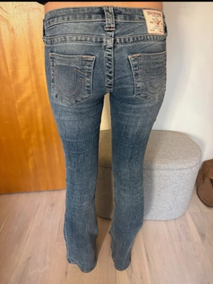 Blå bootcut jeans från True Religion - Jätte fina helt oanvända true religion jeans med ljusrosa summar i storlek 28. Beställde två olika storlekar, då jag var osäker på vilken som skulle passa mig bäst. Så jeansen som syns på bilden är i storleken som jag valde att behålla. Men jeansen som är i storlek 28 är i oöppnad förpackning.