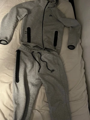 Gråa mjukisbyxor från Nike - Säljer ett par gråa mjukisbyxor från Nike med svarta detaljer och dragsko i midjan. Byxorna har smal passform, muddar vid bensluten och en svart Nike-logga på vänster lår. Perfekta för chill eller träning.