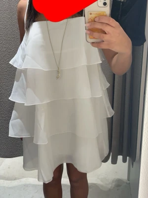 Vit volangklänning - Säljer en söt vit klänning med flera lager volanger och tunna axelband. Klänningen har en luftig och flowy passform, perfekt för varma dagar.