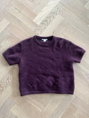 Plommonlila stickad tröja Gina Tricot - Mysig plommonlila stickad tröja från Gina Tricot med korta ärmar och rund halsringning. Tröjan har en lite boxig passform och är gjord i ett fluffigt, mjukt material som känns skönt mot huden. Perfekt för lager-på-lager-stil. Knappast använt den!