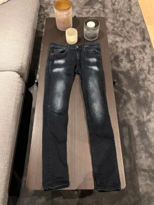 Replay Jondrill mörkblå - Snygga mörkblå slim fit jeans från Replay med slitna detaljer och klassisk femficksdesign. Jeansen har en något tvättad look med ljusare partier på låren och knäna. Perfekta för en trendig och avslappnad stil. Väldigt trendiga just nu! Storleken är W31 L34. 