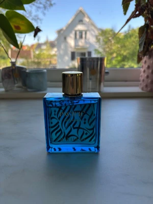 Blå parfymflaska från Rasasi - Snygg parfymflaska från Rasasi i en fyrkantig design med klarblått glas och dekorativa svarta mönster. Flaskan har en elegant guldfärgad kork som ger en lyxig känsla. Perfekt för dig som gillar unika och stilrena doftflaskor. Priset kan diskuteras vid snabb affär 