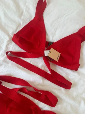 Röd bikini med knyt från Candypants - Snygg röd bikini från Calzedonia med trendiga knytband både upptill och nedtill. Bikinin har trekantsformad överdel och matchande underdel med extra band för en cool look. Perfekt för sommaren och strandhäng!  ÖVERDELEN ÄR I STORLEK 42 OCH UNDERDELEN I STORLEK 38