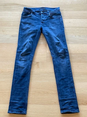 Nudie - Mörkblåa/svarta slim fit nudies i modellen grim tim. De har två små lagningar, en vid låret och en vid andra knät, men utifrån det inga defekter alls. Skriv gärna vid funderingar!