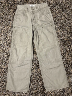 Beige cargobyxor från Xanvas - Stilrena beige cargobyxor från Xanvas med raka ben och flera praktiska fickor framtill. Byxorna har en avslappnad passform och är tillverkade i ett slitstarkt bomullsmaterial. Perfekta för en chill och trendig look.
