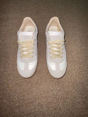 MM gats - Snygga sneakers i vitt och beige med klassisk retrostil. Ovandelen är i en mix av mocka och slätt material, med beige snören och en ljusbrun gummisula. Perfekta för dig som gillar minimalistisk och clean look.