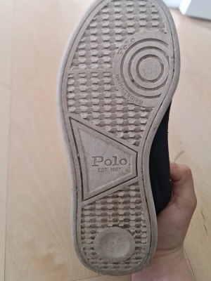 Polo Ralph Lauren sneakers i blå mocka - Snygga sneakers från Polo Ralph Lauren i blå mocka med klassiskt rutigt innerfoder och vita sulor. Skorna har mörkblå snörning och detaljer, samt Polo-logga på innersulan. Perfekta för en stilren och sportig look.