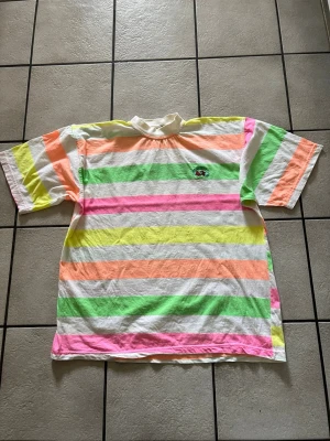 FRUIT OF THE LOOM flerfärgad t-shirt storlek XL i bomull  - Färgglad t-shirt med breda ränder i grönt, rosa, orange, gult och vitt. T-shirten har korta ärmar, rund hals och ett litet broderat märke på bröstet. Tillverkad i mjuk bomull, perfekt för en chill och lekfull stil.