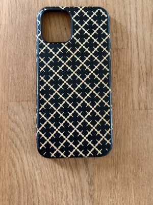 Svart mobilskal By Malene Birger - Snyggt svart mobilskal från By Malene Birger med beige grafiskt mönster. Skalets material är troligtvis plast och det har en stilren, rektangulär form med rundade hörn. Passar perfekt för dig som vill ha ett trendigt och skyddande skal till din mobil.