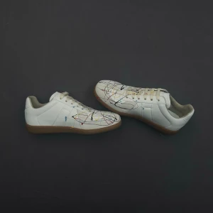Vita Maison Margiella Gats med paintsplatter - Maison Margiela sneakers i vitt läder med unik paintsplatter. Klassisk låg modell med beige gummisula och vita skosnören. Snygg och kreativ design som sticker ut i mängden. Skorna passar både 42 och 43