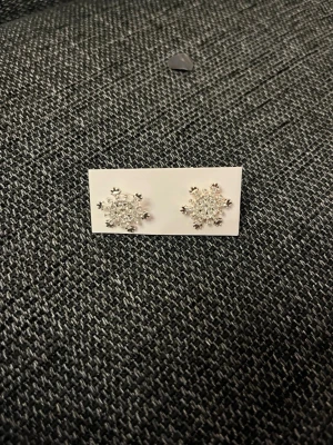 Silvriga snöflingeörhängen - Ett par silvriga örhängen i form av snöflingor med gnistrande stenar. Perfekta för dig som gillar vinterinspirerade accessoarer och vill ha något som glittrar lite extra. Säljs på originalkortet.