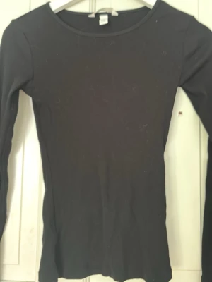 Svart långärmad topp från H&M - En svart, tight långärmad topp från H&M i ribbad bomull. Perfekt att styla med jeans eller kjol för en enkel och clean look. Klassisk rund halsringning och figurnära passform.