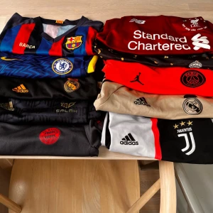 Blandade fotbollströjor från toppklubbar - Säljer ett gäng snygga fotbollströjor från klubbar som Barcelona, Chelsea, Real Madrid, Liverpool, PSG, Bayern München och Juventus. Tröjorna har klubbmärken, sponsorer och är i olika färger som röd, blå, svart, beige och vit. Perfekta för dig som älskar fotboll och vill ha stil på planen. Alla tröjor är 8 till 11 år. 70kr styck 