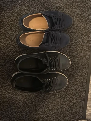 Svarta sneakers  Lanvin och Louboutin mörkblå  - Två par svarta sneakers, ett par från Lanvin med vit sula och klassisk design, samt ett par från Louboutin med röd sula och stilren look. Båda paren har lågt skaft och snörning framtill. Perfekta för en clean och stilren outfit låda för Louboutin finns men en separat låda för lanvins  skorna passar både 41 42 
