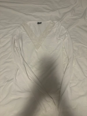 Vit långärmad topp med spets V-ringning - Supersöt vit långärmad topp från Gina Tricot med djup V-ringning dekorerad med spetsdetaljer. Perfekt att styla med jeans eller kjol för en fräsch look. Mjuk och skön känsla tack vare bomullsmaterialet.