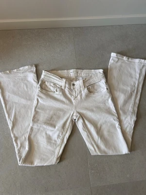 Vita bootcut jeans från Gina tricot  - Säljer ett par vita low waist bootcut jeans från Gina Tricot med klassisk femficksmodell och broderade bakfickor. Jeansen har normal midja och är tillverkade i ett mjukt denimtyg med lite stretch. Perfekta för en clean och fräsch look. Små missfärgningar/slitage längst ner på benen från användning, se sista bilderna. 