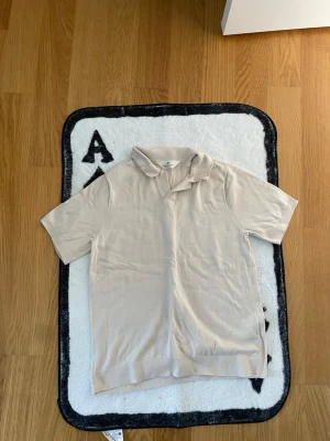 Beige kortärmad polotopp - Stilren beige polotopp från H&M med korta ärmar och klassisk krage. Toppen är tillverkad i mjuk bomull och har en relaxed fit som passar perfekt till många olika looks.