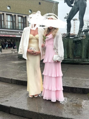REDAN KÖPT! - Elegant långklänning i ljusgul nyans med sweetheart-ringning och smala axelband. Klänningen har en figurnära passform och är tillverkad i ett glansigt material som ger en lyxig känsla. Perfekt för speciella tillfällen.