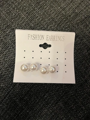 Pärlörhängen i silverfärg, 2 par - Två par klassiska pärlörhängen i vit och silverfärg. Runda studs med glansig yta, perfekta för en stilren look. Kommer på originalkort med texten 'Fashion Earrings'.