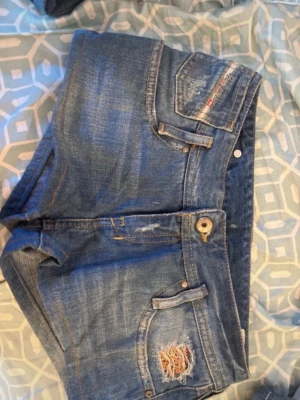 Blå diesel jeansshorts med slitning och low waist - Snygga blå jeansshorts från Diesel slitning på ena fickan framtill. Shortsen är low waisted och är perfekta för sommardagar och en avslappnad stil. Köpte det från Kanada i en 2000s vintage affär!