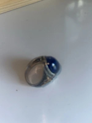 Arabisk silver ring med blå sten - Säljer en snygg silverfärgad ring med en stor, rund blå sten i mitten. Ringen har detaljerade mönster längs sidorna som ger en cool vintagekänsla. Perfekt för dig som vill sticka ut med en unik accessoar.