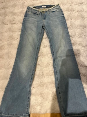 Ljusblå bootcut jeans från Nelly  - Snygga ljusblå bootcut jeans från Nelly, med fransad midja och klassisk femficksdesign. Jeansen har en lätt tvättad look och vida ben, perfekta för en avslappnad och trendig stil.