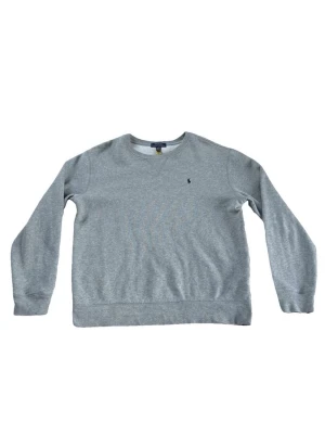 Polo Ralph Lauren Sweater - Snygg grå stickad tröja från Polo Ralph Lauren med rund halsringning och broderad logga på bröstet. Tröjan har ribbade muddar vid ärmslut och nederkant, perfekt för en avslappnad och stilren look.