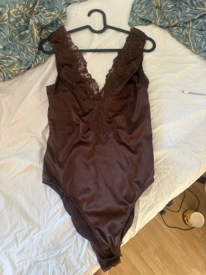 Brun Zara spetsbody - Snygg brun body i satin material med djup V-ringning och dekorativa spetsdetaljer framtill.  Endast testad 