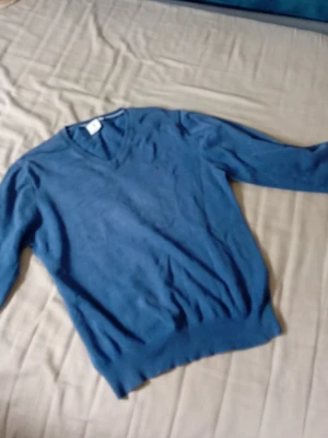 Blå V-ringad tröja från Boomerang - Snygg blå V-ringad tröja från Boomerabg med diskret logga broderad på bröstet. Tillverkad i mjukt material som känns skönt mot huden. Perfekt att bära över en skjorta eller t-shirt för en clean look.