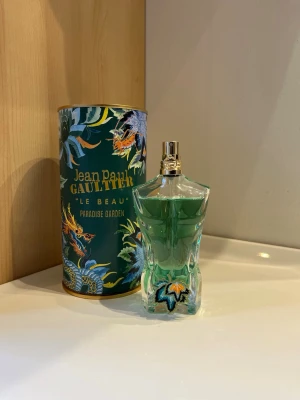 Jean Paul Gaultier Le Beau Paradise Garden - Perfekt parfym nu till sommaren🔥🔥🔥Jean Paul Gaultier Le Beau Paradise Garden parfym med en unik flaska formad som en manlig torso i genomskinligt glas med grön vätska. Flaskan har en dekorativ palm och guldigt sprayhuvud. Kommer med en färgglad, tropisk förpackning.