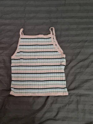 Randig ribbad linnetopp från H&M - Säljer en söt randig linnetopp från H&M i pastellfärger med smala axelband. Toppen är ribbad och har rosa, blå, grå och svarta ränder. Perfekt för varma dagar och enkel att matcha med jeans eller shorts.