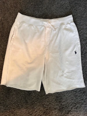 Vita shorts från Polo Ralph Lauren - Snygga vita shorts från Polo Ralph Lauren med klassisk broderad logga i marinblått på benet. Shortsen har snörning i midjan och är tillverkade i mjuk bomull, perfekta för sommardagar. Två sidofickor och relaxed passform. 