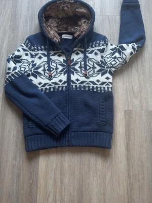 Blå stickad hoodie från pier one - Mysig blå stickad hoodie med vitt nordiskt mönster över bröst och armar. Dragkedja framtill, två fickor och ribbade muddar. Huva med brun fuskpälsfoder och dragsko med läderdetaljer. Perfekt för kyligare dagar! Använd 2-3 gånger, säljer pga att den inte passar mig. Skick 10/10. Hör av dig vid intresse!😀