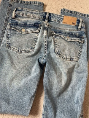 Ljusblå raka jeans från 157 - Säljer ett par ljusblå jeans från 157 med raka ben och klassiska bakfickor med lock och knapp. Jeansen har en avslappnad passform och är tillverkade i denim med snygg tvättad look. Perfekta för en casual stil.