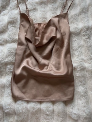  satintopp - Snygg linnetopp i champagnefärgad satin med tunna axelband och draperad urringning. Perfekt att styla med jeans eller kjol för en trendig look.