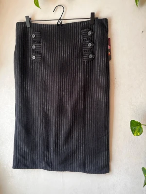 Pennkjol kritstrecksrandig  - Kritstrecksrandig pennkjol i linne/bomullsblandning. Gith/gothica. Mörkblå/nästintill svart.   Från rock/goth-märket Adeline   Mått:  Midja: 44cm  Längd: 68cm  Aldrig använd, prislapp kvar. Inköpt på Redrum i Gävle ca 2010. Nypris 499kr (hade förmodligen varit betydligt högre idag).   Se även andra annonser för bundle! 🌷  Avhämtning i Gävle/Uppsala går att lösa (skriv pm innan köp)