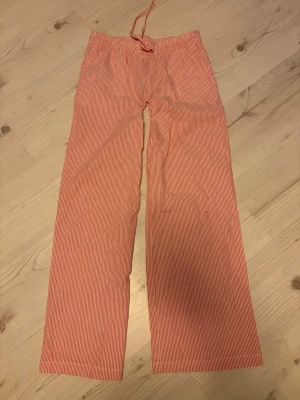 Randiga pyjamasbyxor från hm - Säljer ett par snygga pyjamas byxor från hm i rödvitt randigt mönster. Byxorna har raka ben, resår och dragsko i midjan för skön passform. Perfekta för en avslappnad och trendig stil. Materialet är 100% bomull.
