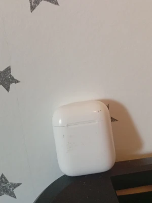 Apple AirPods med laddningsetui - Säljer ett par vita Apple AirPods med tillhörande laddningsetui. De är trådlösa och har en stilren, minimalistisk design i plast. Perfekta för musik, poddar och samtal på språng. Laddningsetuiet är kompakt och lätt att ta med sig. Den vänstra AirPoden har dålig batteritid men det är inget fel på den högra AirPoden.