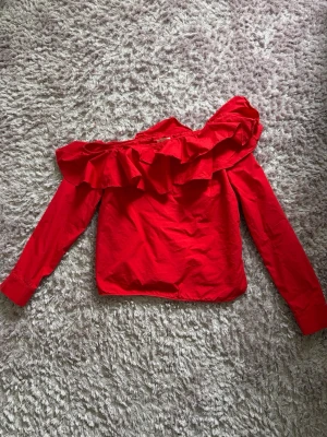 Röd offshoulder topp med volang - Trendig röd offshoulder topp med volang längs överdelen och långa ärmar. Perfekt för dig som vill sticka ut med en färgstark och snygg look. Tillverkad i mjuk bomull som känns skön mot huden.