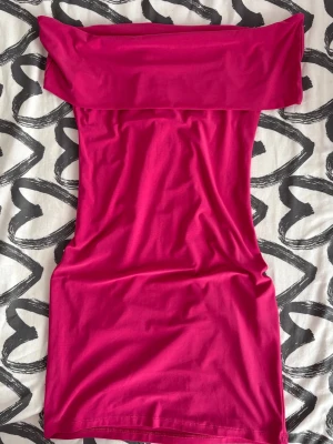 Rosa offshoulder kortklänning - Trendig rosa kortklänning med offshoulder-design och figurnära passform. Klänningen är enkel och stilren, perfekt för dig som gillar en färgstark look. Tillverkad i mjukt och stretchigt material för extra komfort.