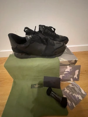 Svarta sneakers från Valentino - Snygga svarta sneakers från Valentino med coola detaljer och blandning av mocka och läder. Skorna har en klassisk låg siluett, svarta skosnören och diskret logga på sidan. Kommer med originalkartong, dustbag och extra skosnören.