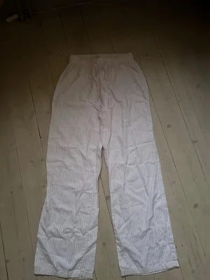 Rosa pyjamasbyxor med vita ränder - Pyjamasbyxor i rosa med tunna, vita ränder. Byxorna har rak passform, resår i midjan och dragsko för extra komfort. Perfekta för mysiga hemmakvällar. Materialet känns mjukt och luftigt mot huden.